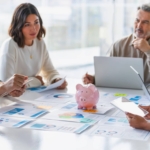 marketing team seated at conference table budget paperwork and piggy bank in center of table